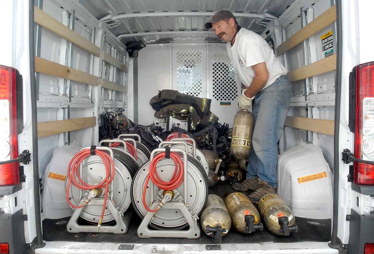 Jordan Pollack, regional representative for Firefighters Crossing Borders, loads the back of a utility van with used breathing apparatus air packs donated to his organization Wednesday by the Port Angeles Fire Department. (Keith Thorpe/Peninsula Daily News)