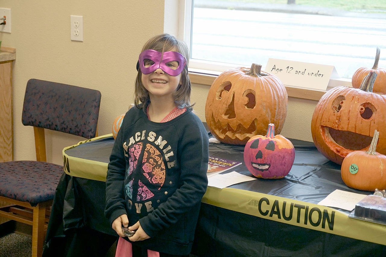 A masked girl shows off her pumpkin at the Clallam Bay Library’s annual pumpkin decorating and carving contest in 2015. (North Olympic Library System)