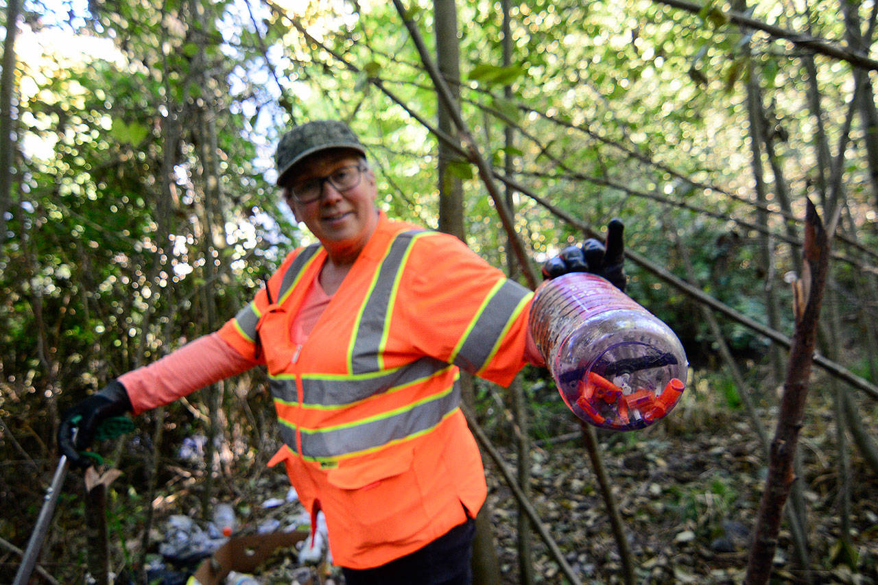 Deana Volker holds up a bottle of used syringes she found while cleaning an abandoned camp on Tumwater Creek on Oct. 15. (Jesse Major/Peninsula Daily News)