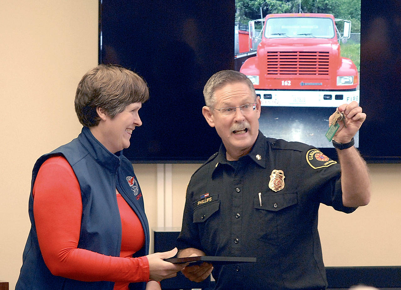Sam Phillips, chief of Clallam County Fire District No. 2, right, holds up the keys to a refurbished brush truck used for fighting wildland fires after receiving them from Julie Knobel, assistant regional manager for the state Department of Natural Resources, during a ceremony in Port Angeles. The truck, shown on the screen in the background, was acquired by the department through a DNR surplus program that allocates used firefighting equipment to local agencies around the state. (Keith Thorpe/Peninsula Daily News)