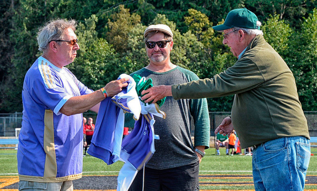 As Super Cup co-organizer Tim Tucker (center) looks on, Sequim’s Brandino Gibson, left, and Port Angeles mayor Patrick Downie exchange jerseys at the 2016 Super Cup. This year’s event is set tonight (Friday, Oct. 27) at Civic Field.