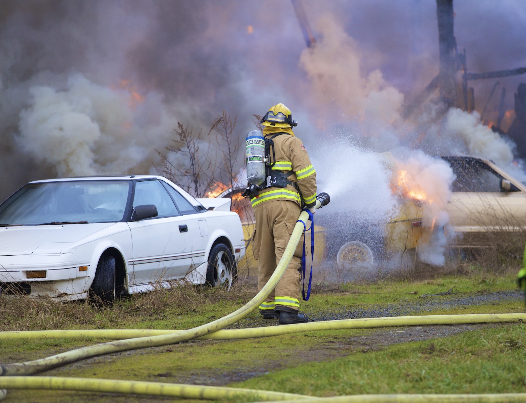 A firefighter from Station 91 on Indian Island hoses down a burning car at a barn fire in Chimacum on Saturday afternoon. (Steve Mullensky/for Peninsula Daily News)