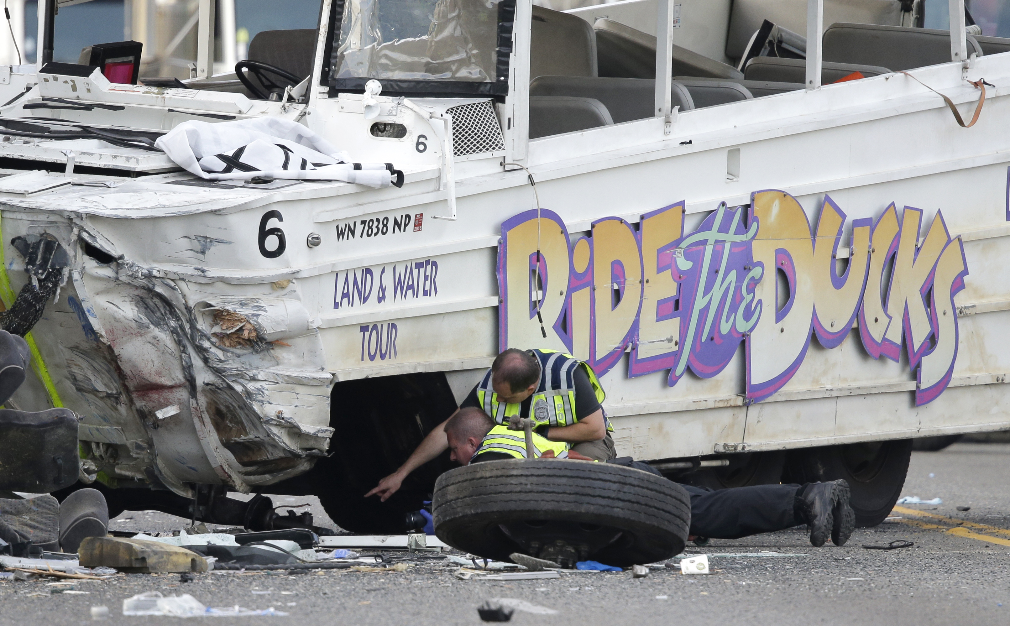 Seattle Police officers look under a "Ride the Ducks" tourist vehicle as a tire and wheel from the bus sits nearby before the bus is loaded onto a flatbed tow truck Thursday following a fatal crash with a charter passenger bus earlier that day in Seattle. The Associated Press