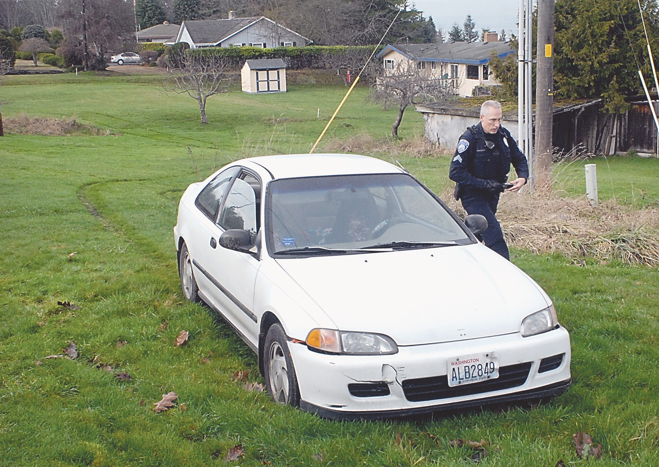 Port Angeles Police Cpl. David Dombrowski examines a car that was driven through backyards and then abandoned behind 1723 Lambert Lane after a short chase in Port Angeles on Thursday.  Photo by Keith Thorpe/Peninsula Daily News ()