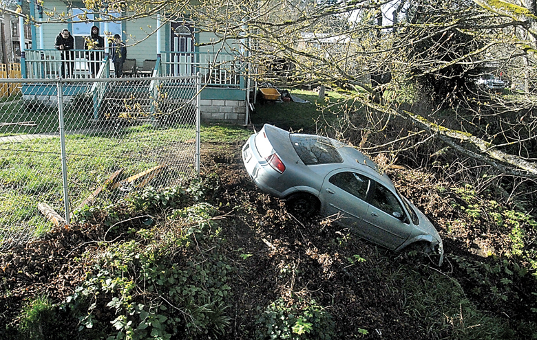 A car sits partially over the embankment dropping down into Valley Creek near the eastern Eighth Street bridge on Wednesday while being pulled by a tow truck after the driver crashed through a fence and across a front yard. (Keith Thorpe/Peninsula Daily News)