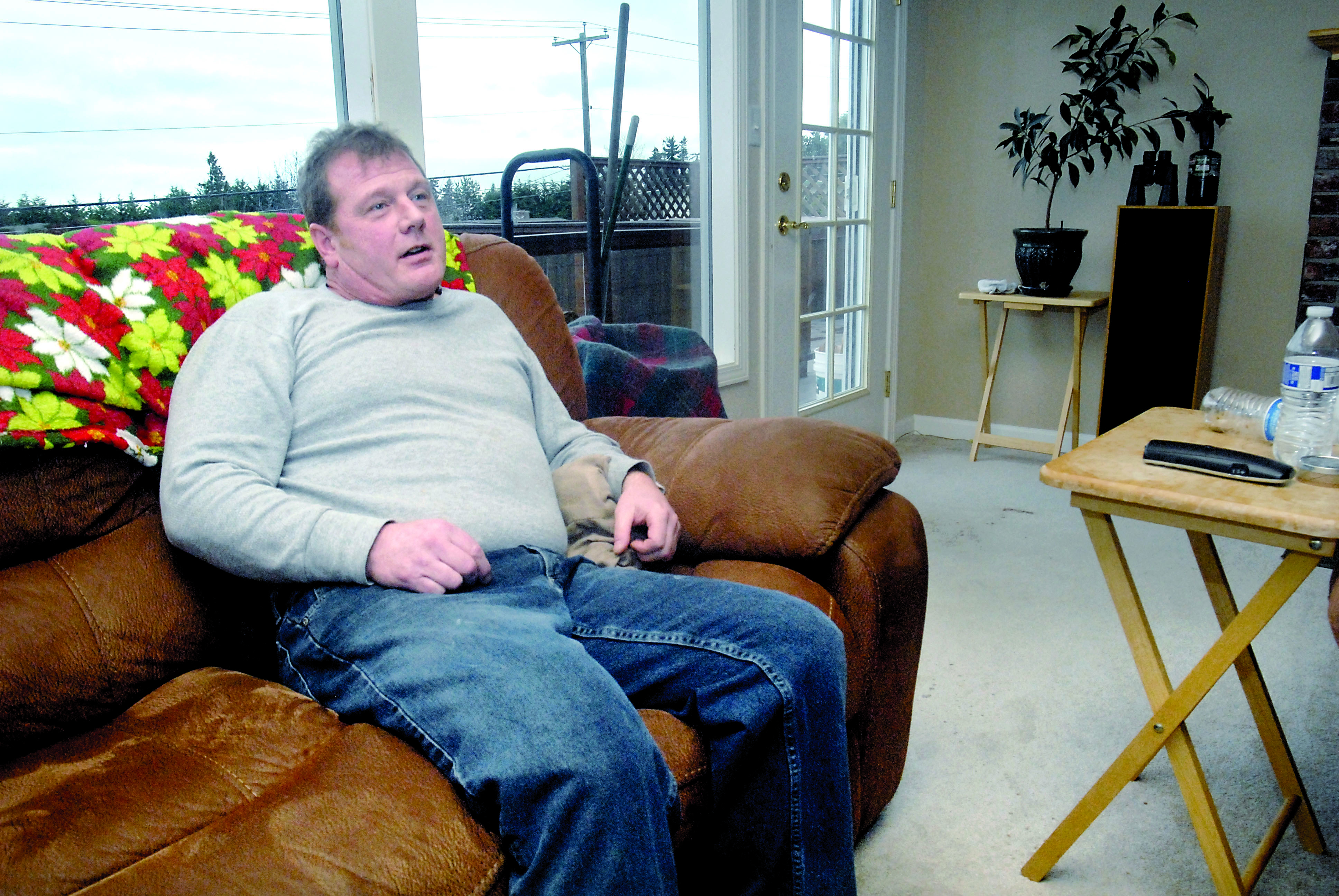 Eric Edmiston sits on the couch of his Port Angeles home near the door where a Port Angeles police dog attacked him. (Keith Thorpe/Peninsula Daily News)