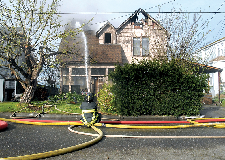 Port Angeles firefighter Tim Davis sprays water on a burning house at 715 E. Caroline St.