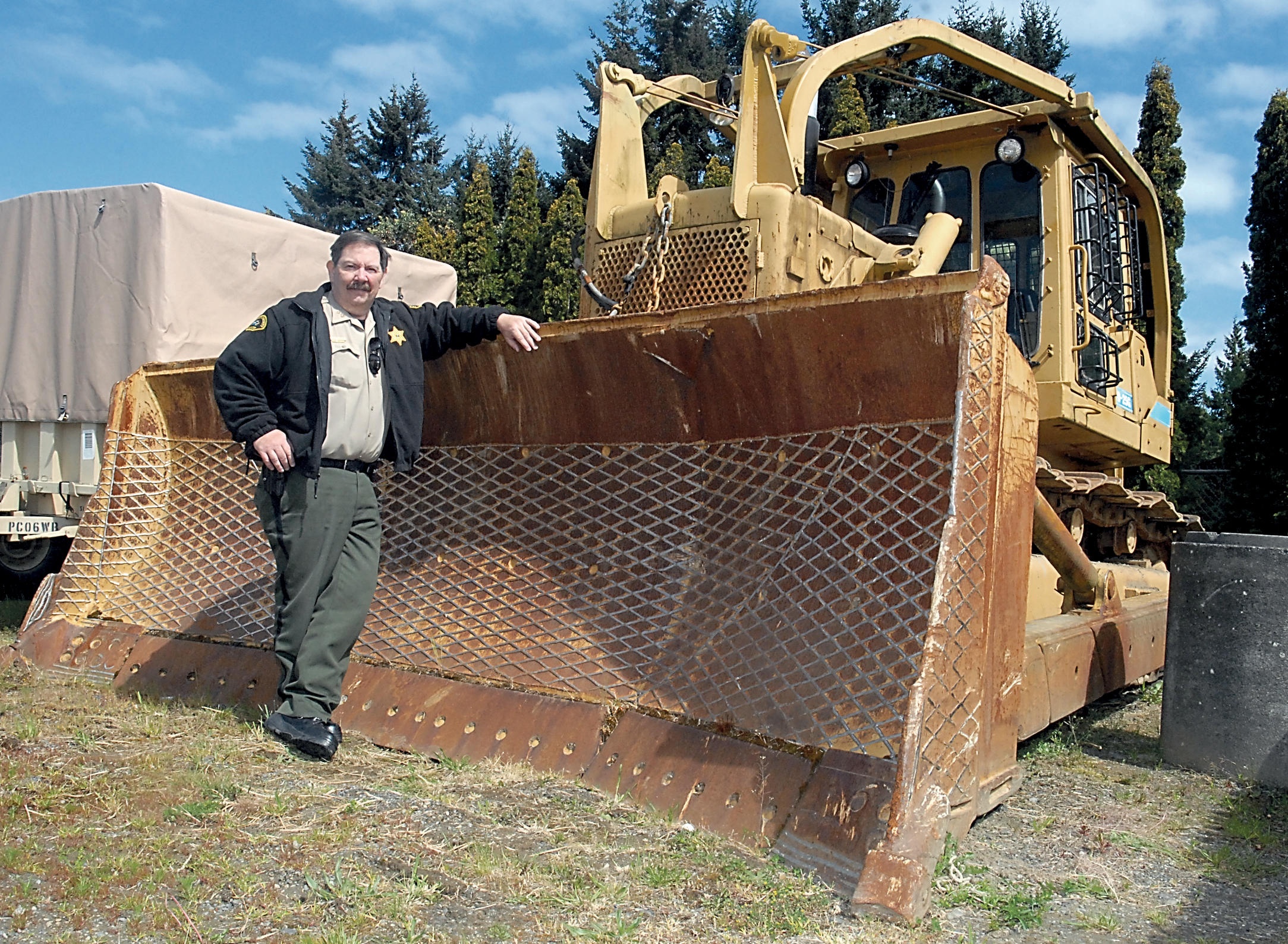 Clallam County Undersheriff Ron Cameron stands with the logging bulldozer that was used during the May 10