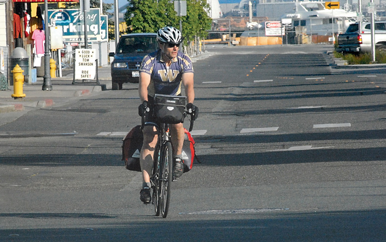 Bicyclist Tom Swanson approaches Port Angeles City Pier on Saturday to start a cross-country bike ride to raise money for the Pathway to Prosperity scholarship fund. (Keith Thorpe/Peninsula Daily News)
