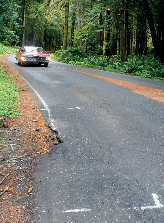 Paint outlines mark a spot of crumbling roadway as a car makes its way towards Lake Crescent Lodge and Bovee’s Meadow at Barnes Point on Lake Crescent in Olympic National Park last week. — Keith Thorpe/Peninsula Daily News ()