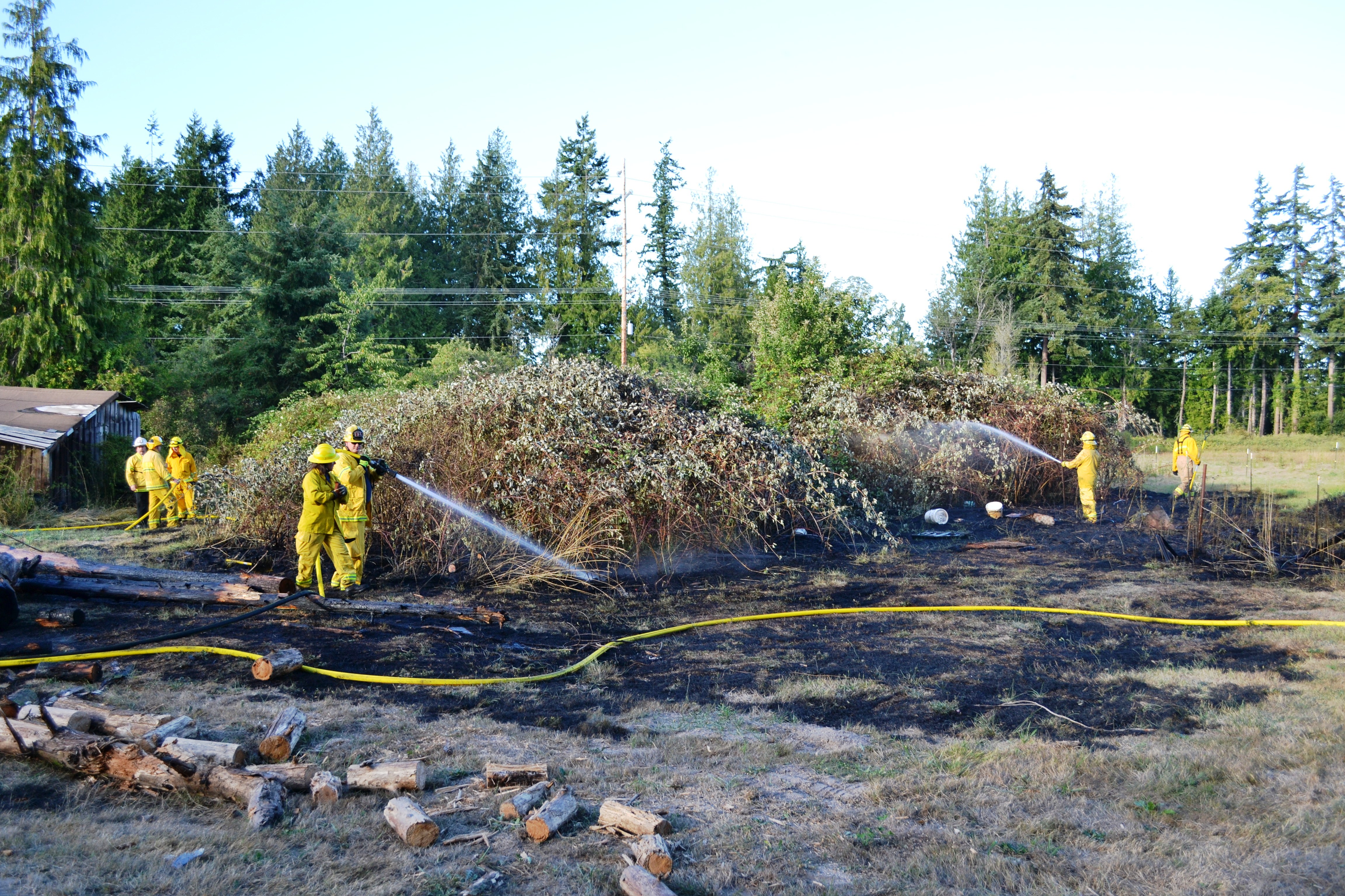 Firefighters with East Jefferson Fire-Rescue and Naval Magazine Indian Island spray down hot spots after extinguishing a brush fire in the 800 block of Four Corners Road in Jefferson County on Sunday. — East Jefferson Fire-Rescue