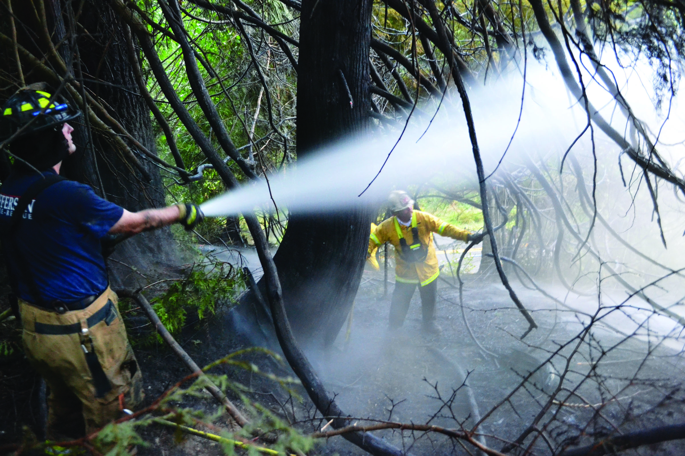 Firefighters hose down a brush fire near Chimacum on Saturday. Power lines sparked the fire in nearby foliage. East Jefferson Fire-Rescue