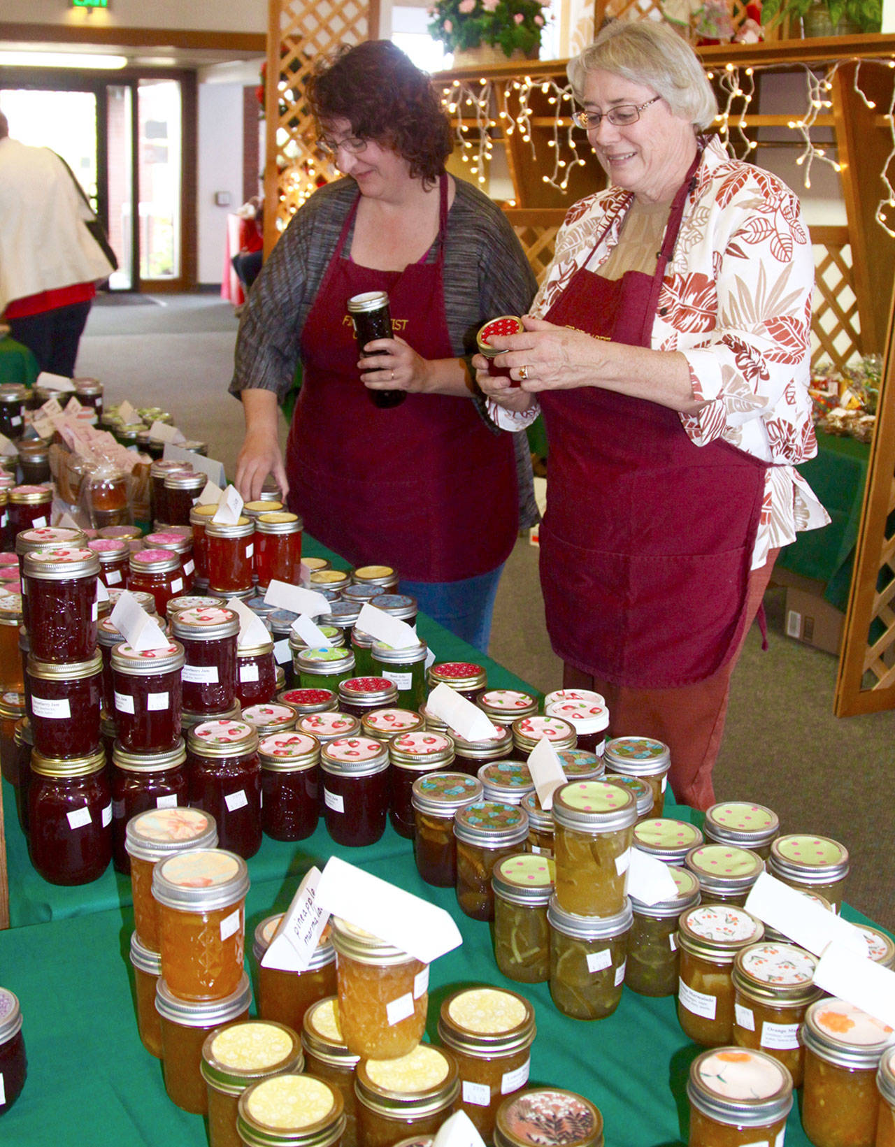 The Christmas Bizarre season is upon us now. Seven organizations have their bizarres this first weekend in November. Pictured here is preparation for the bizarre at the First Baptist Church in 2016. Kim Luker, left, and Robin Sweeney look over the many jars of handmade jams and jellies especially made for the public sale. (Dave Logan/for Peninsula Daily News)