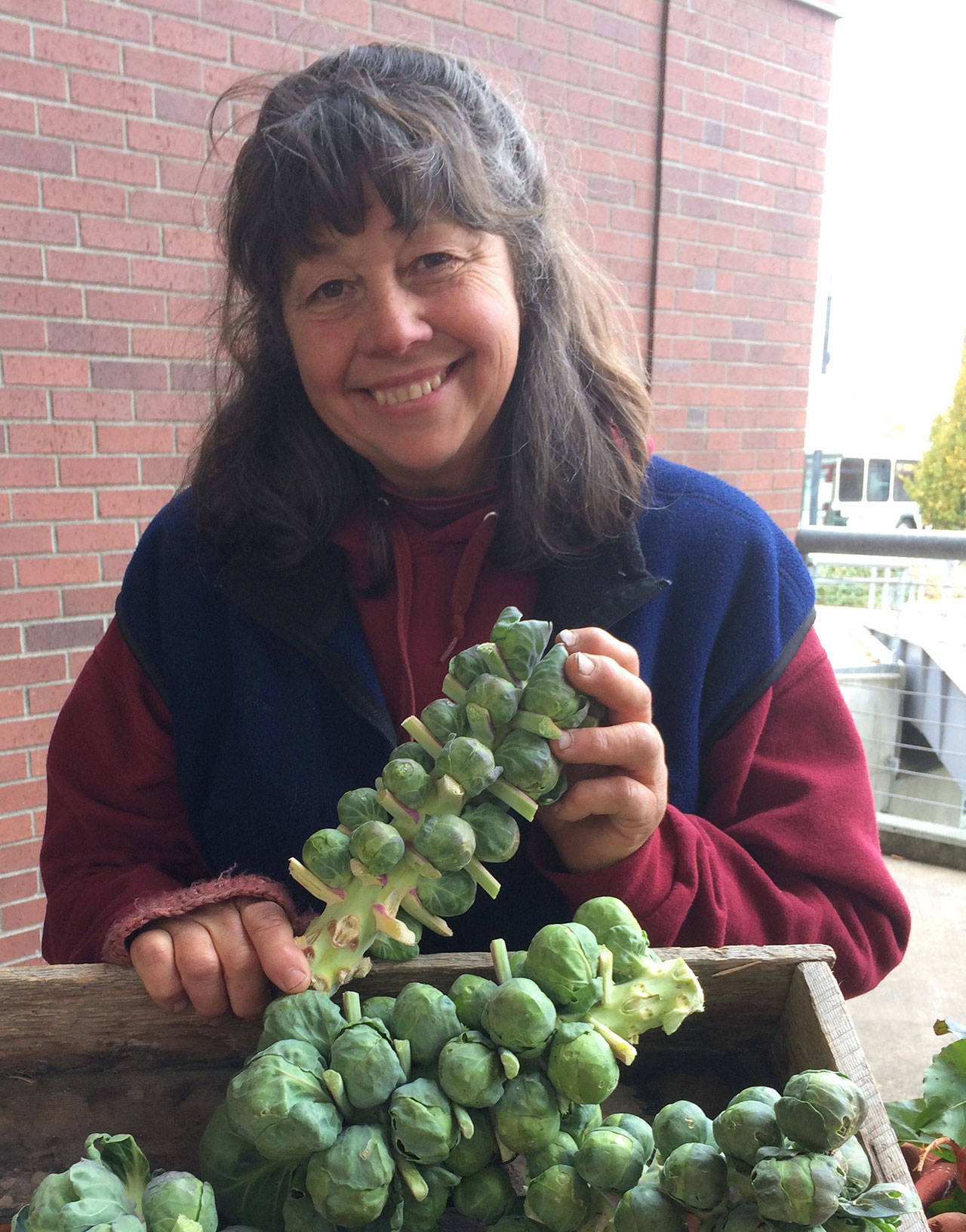 Christie Johnston of Johnston Family Farm holds Brussels sprouts at the Port Angeles Farmers Market. (Betsy Wharton/for Peninsula Daily News)