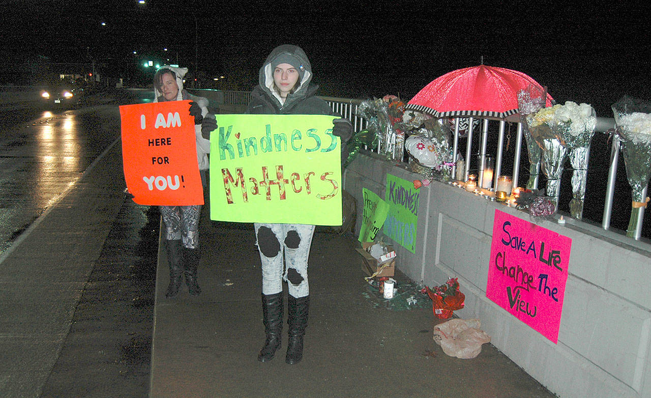 Maariyah Dugan, right, and Siouxzie Hinton stand in the rain last week on the Valley Creek bridge in Port Angeles to protest the lack of suicide barriers on the span and to urge people to be more compassionate to one another. (Paul Gottlieb/Peninsula Daily News)