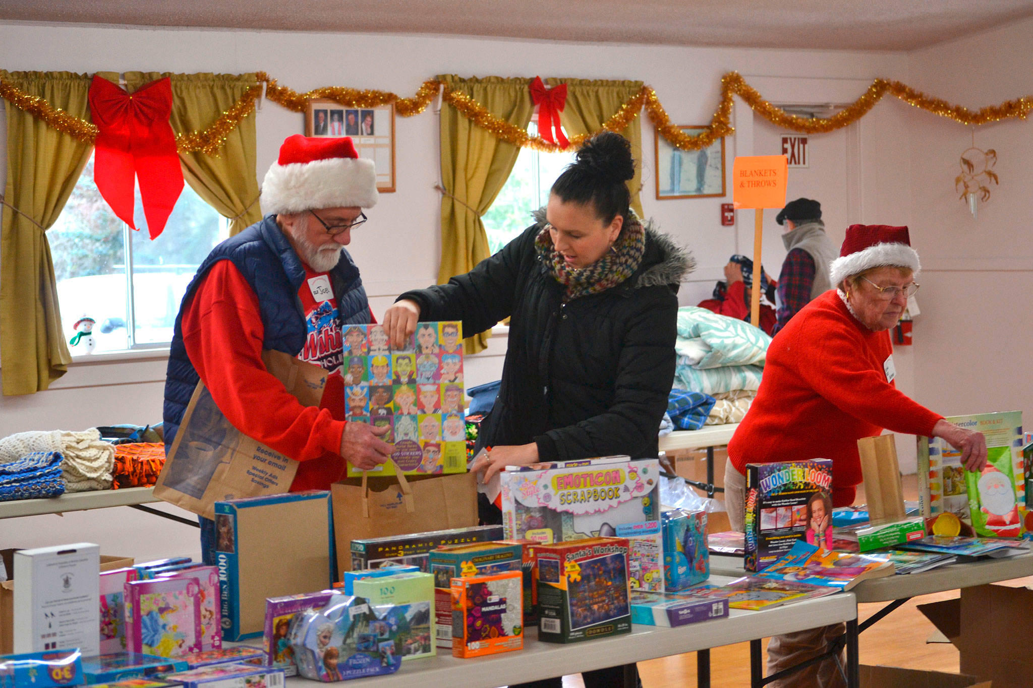 Volunteers Joel Ogden and Anne Notman with Sequim Community Aid help Sheena Touchard, right, look for toys at last year’s Toys for Sequim Kids. Organizers said 400 children in Sequim received items from the event in 2016. This year, the event is set for Dec. 13 at the Sequim Prairie Grange. (Matthew Nash/Olympic Peninsula News Group)