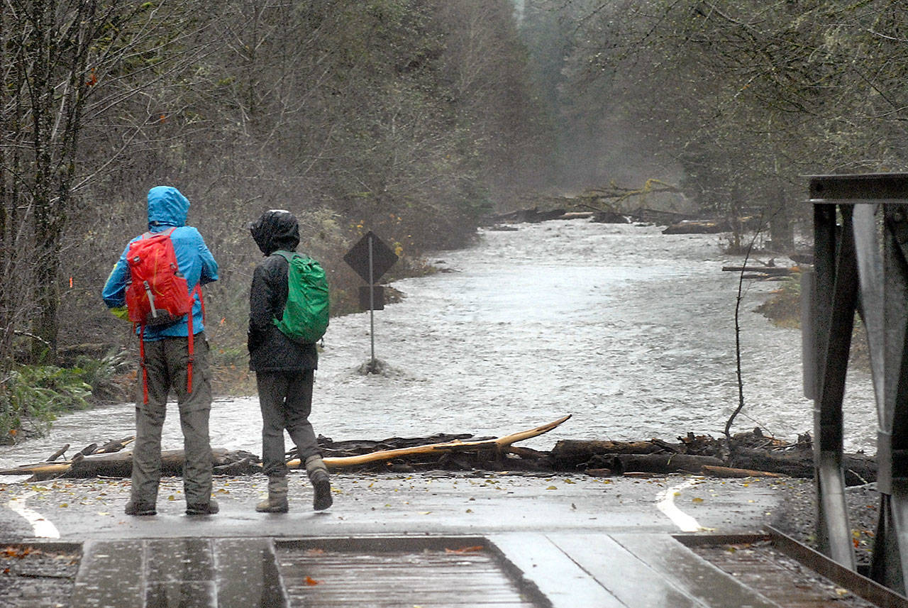 Mark and Ann Underwood of Bremerton look at a side channel of the rain-swollen Elwha River as it floods across Olympic Hot Springs Road near the former Elwha Campground in Olympic National Park on Thursday. (Keith Thorpe/Peninsula Daily News)