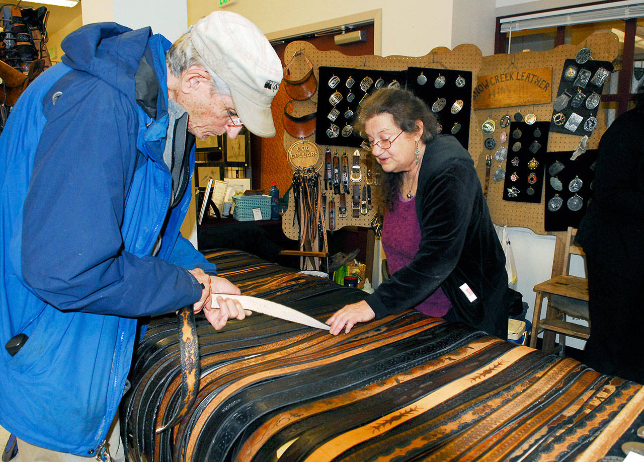 Artist Jenny Preston describes her technique for making leather belts to recent Port Townsend transplant George Stanley. Preston uses knife work, stamping and dyes on her top grain cowhide creations. (Jeannie McMacken/for Peninsula Daily News)