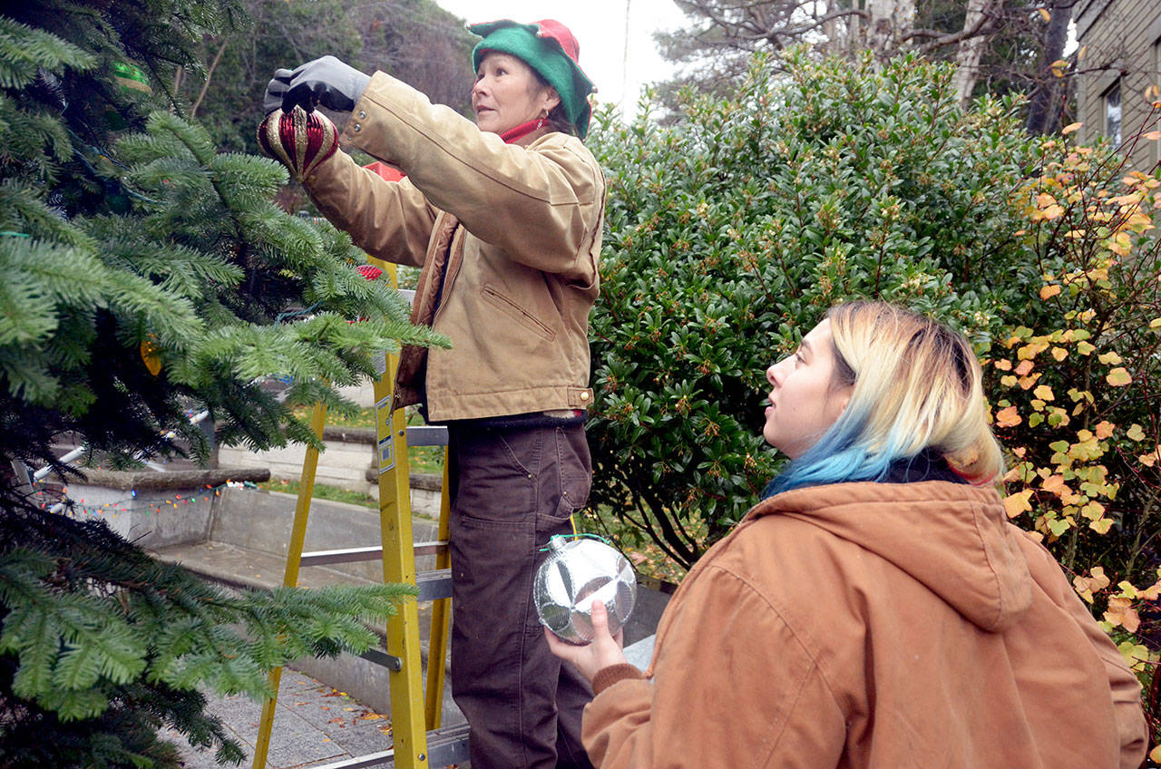 Willow Hundtoft hands ornaments to Tara Homeyer to help decorate the Christmas tree in downtown Port Townsend. The two were part of a handful of volunteers who braved the rain to help decorate the tree Tuesday. (Cydney McFarland/Peninsula Daily News)