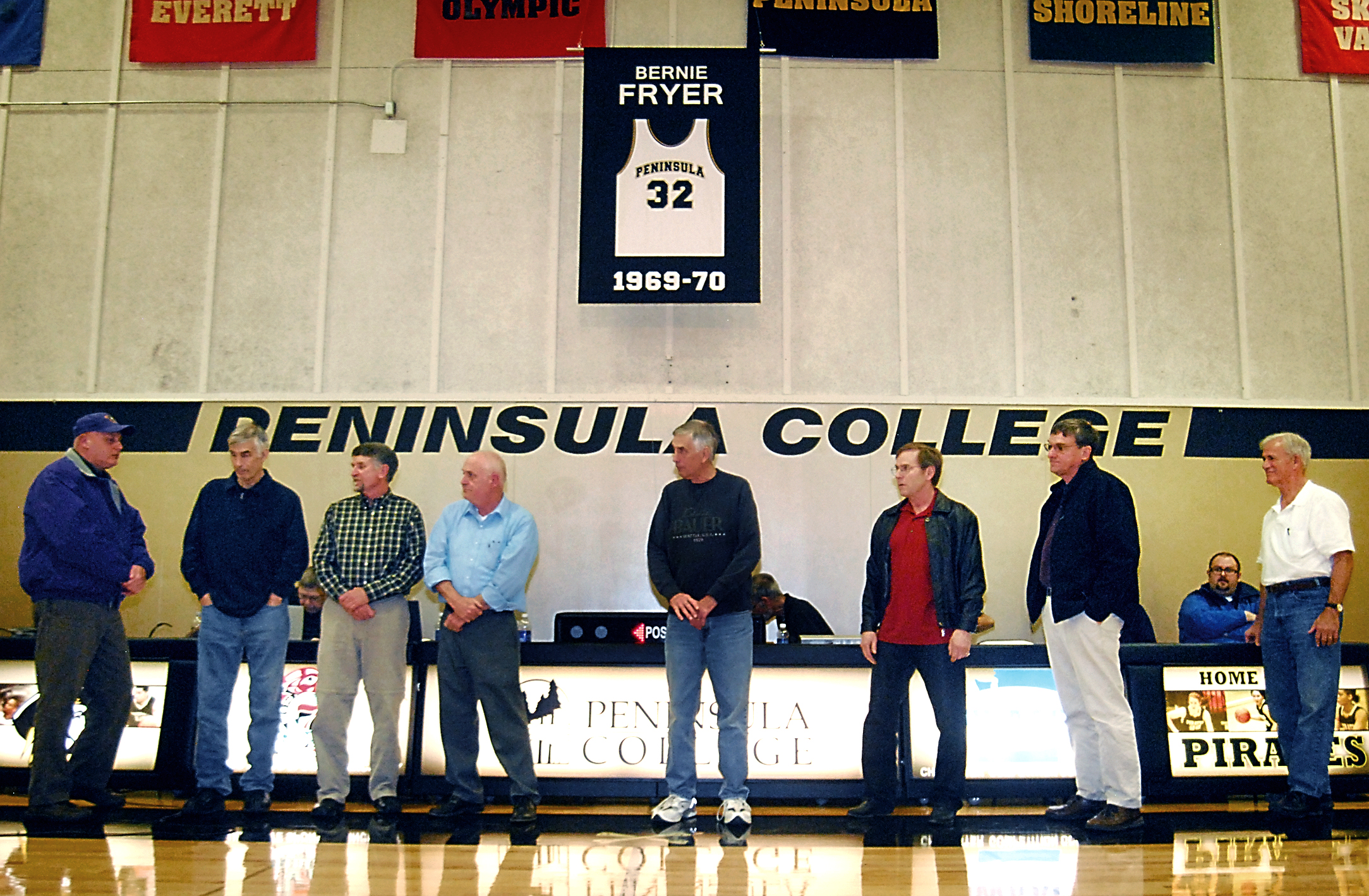 A retired jersey for Bernie Fryer hangs from the ceiling of the Peninsula College gym as members of the 1970 championship team are honored. Pictured are