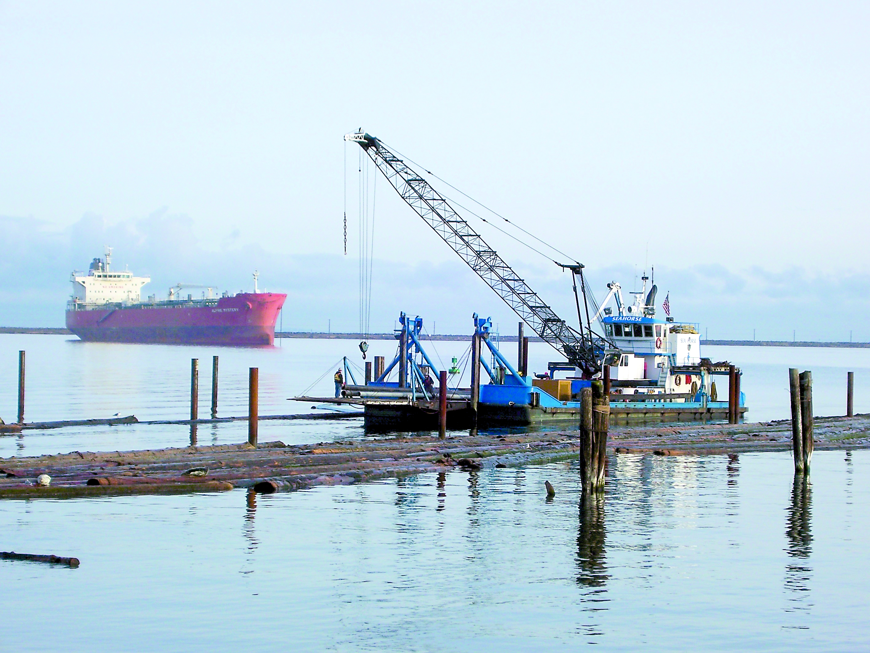 The floating derrick Sea Horse works amid the log booms in Port Angeles Harbor near the Boat Haven breakwater. Thats the oil tanker Alpine Mystery anchored in the harbor at left. -- Photo by David G. Sellars/for Peninsula Daily News