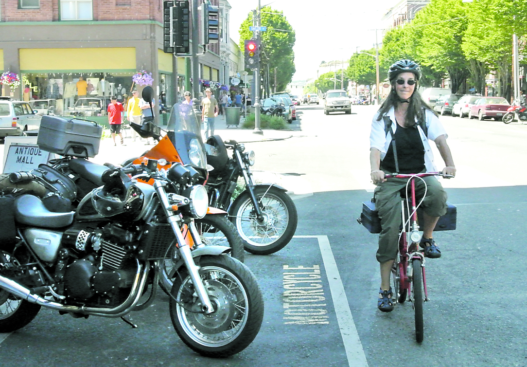 Nancy Frederick rides her bike past the motorcycle space at the corner of Water Street and Taylor Street that will be the temporary site of a rack that can store about a dozen bikes. Charlie Bermant/Peninsula Daily News