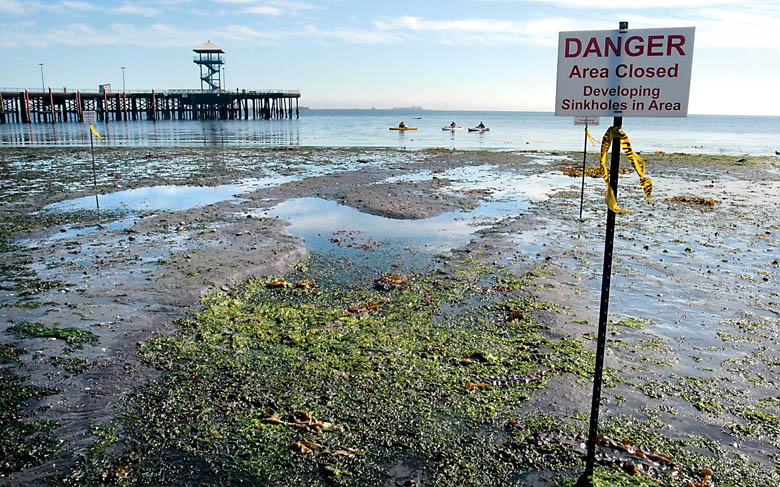 Signs surround a water-filled depression made visible during Saturday morning's minus-2.6 tide at Hollywood Beach in Port Angeles. Keith Thorpe/Peninsula Daily News