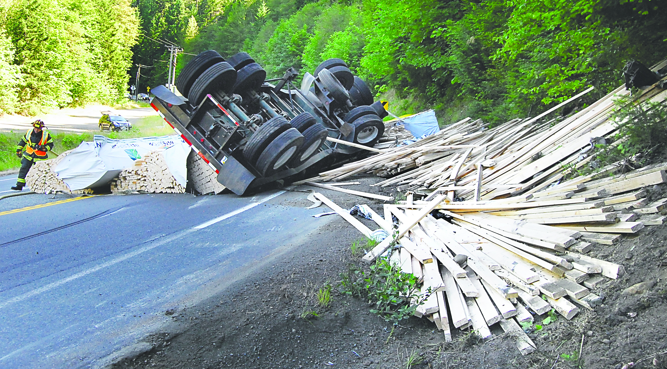 Clallam County Fire District No. 2 Lt. Kevin Thompson pulls a fire hose around the scene of an overturned semi-trailer combination carrying lumber on U.S. Highway 101 at Olympic Hot Springs Road this morning. Keith Thorpe/Peninsula Daily News