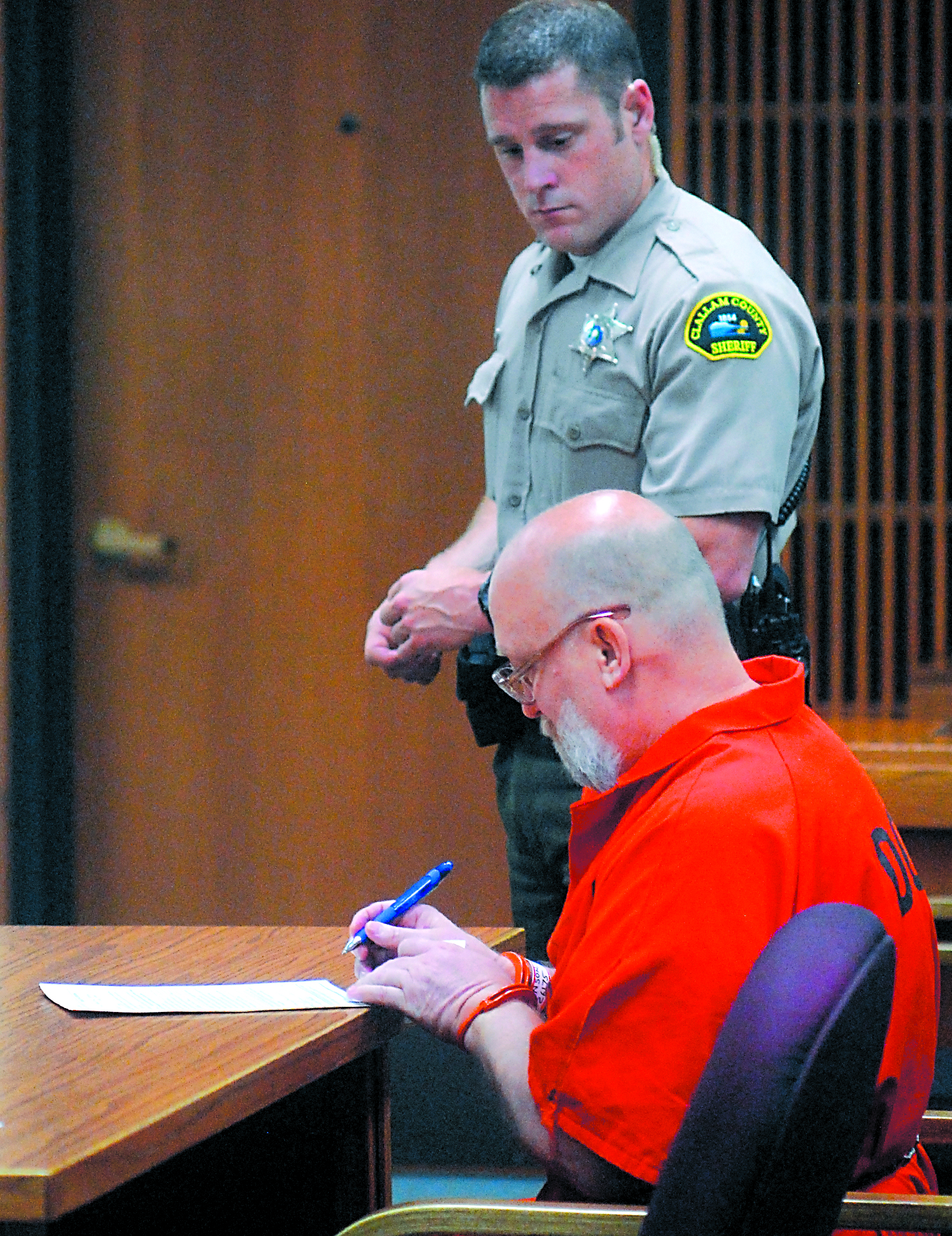 Darold Stenson signs court papers during last Friday's status hearing in Clallam County Superior Court. Standing watch is court sercurity officer Eric Morris. Keith Thorpe/Peninsula Daily News