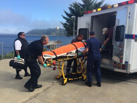 A Coast Guard Station Neah Bay crew member assists local emergency medical services with the transfer of a diver rescued off Cape Flattery. Coast Guard