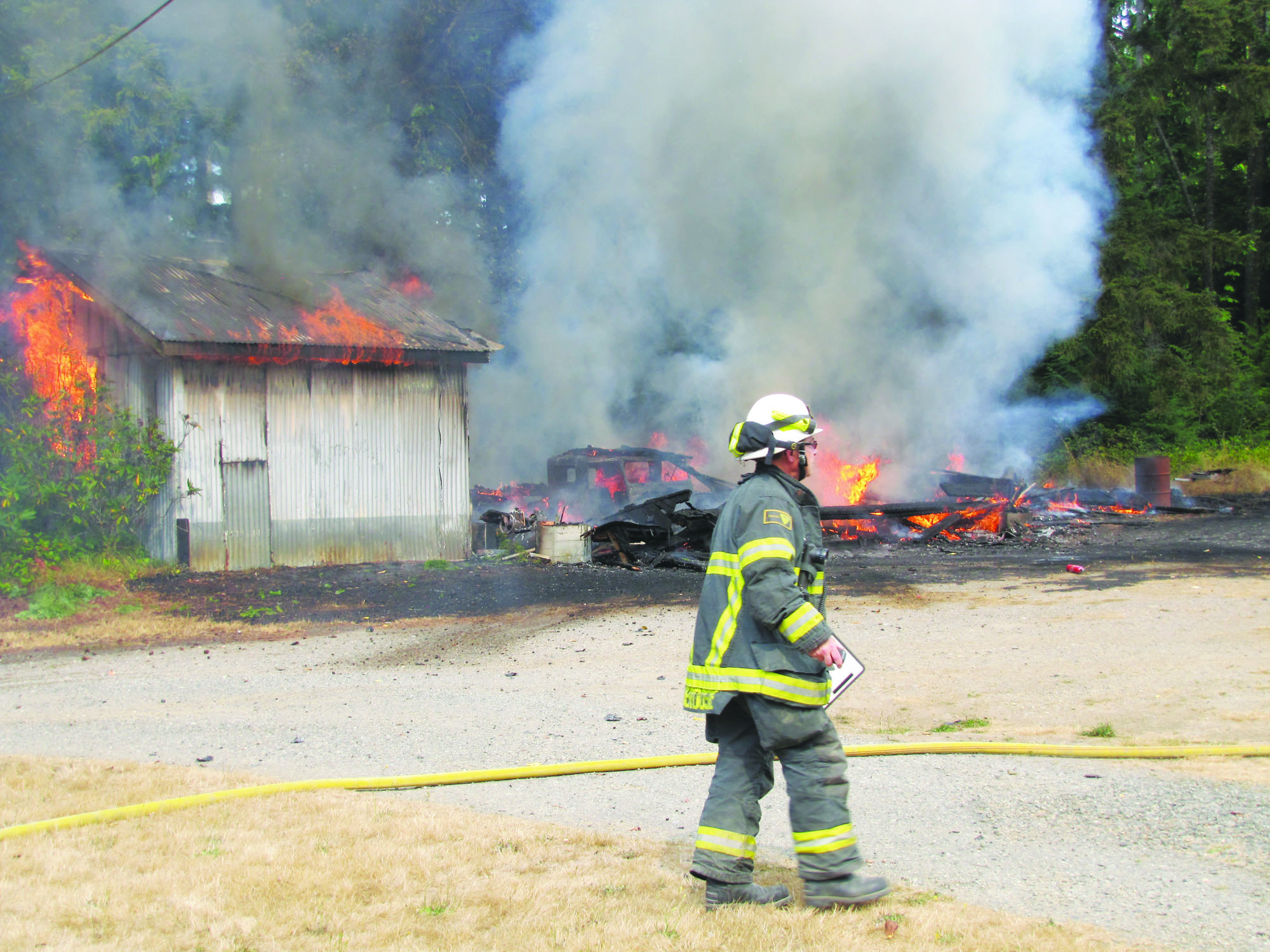 Assistant Chief Mike DeRousie of Clallam County Fire District No. 2 monitors the situation at 721 Benson Road in Port Angeles on Sunday afternoon. Arwyn Rice/Peninsula Daily News