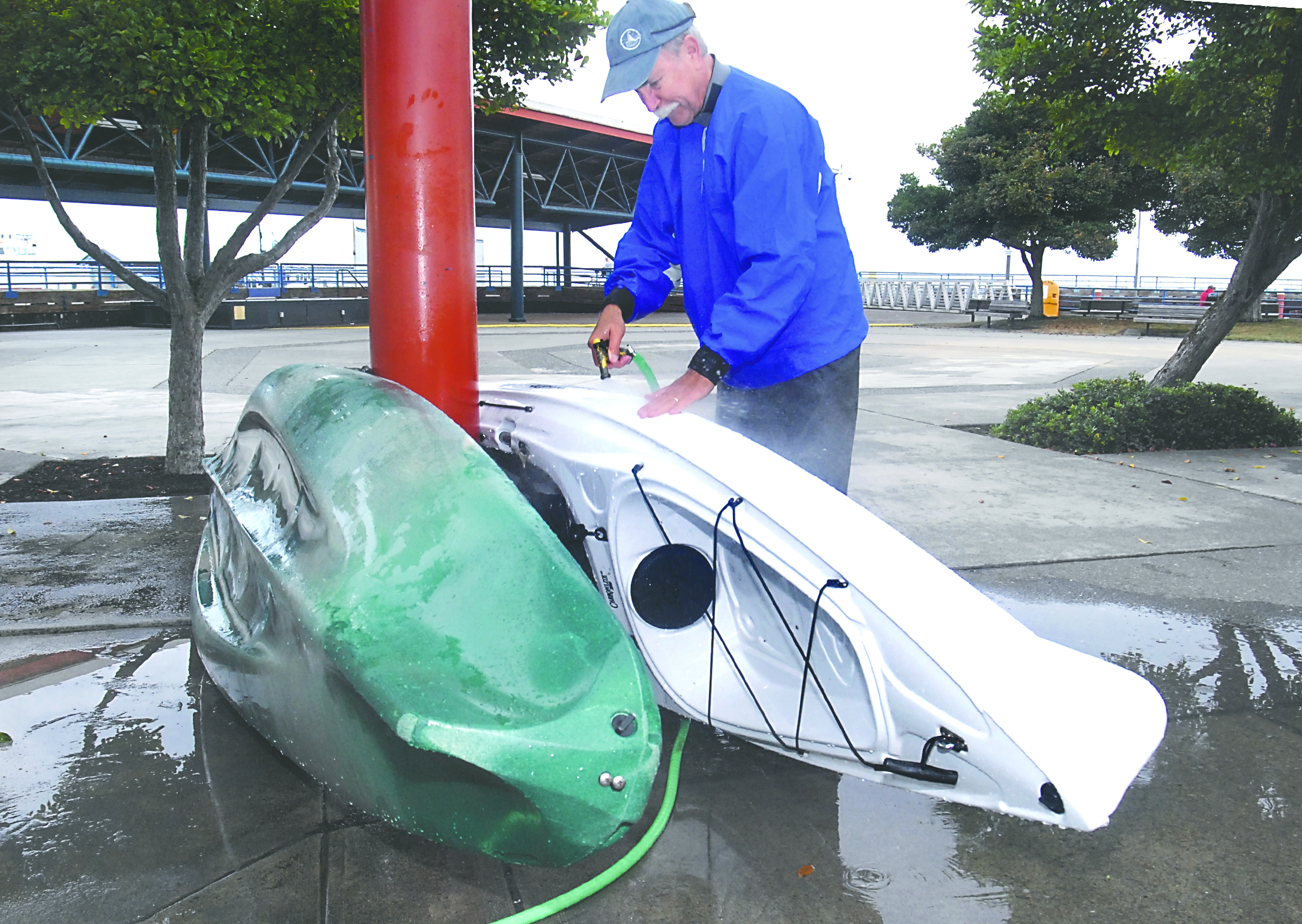 Thad Schroeder of Port Angeles washes residue from the side of a kayak outside the Feiro Marine Life Center on City Pier after paddling through a sheen discovered on Saturday on the surface of Port Angeles Harbor. Keith Thorpe/Peninsula Daily News
