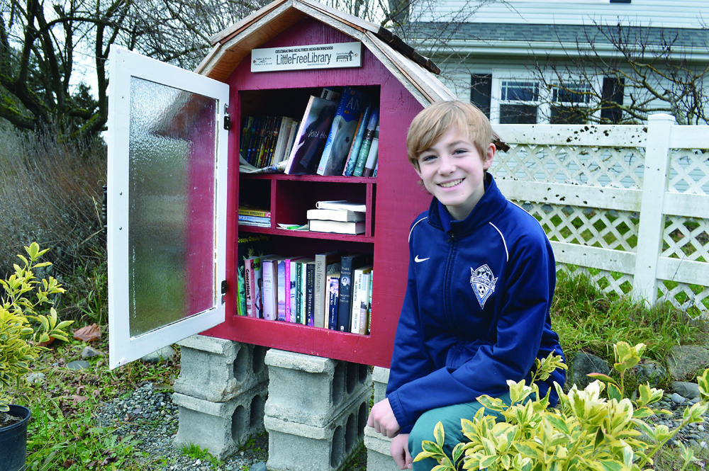 Twelve-year-old Tane Ridle kneels beside the road-side little library he built with his uncle on their family's farm on Kitchen-Dick Road west of Sequim. Joe Smillie/Peninsula Daily News