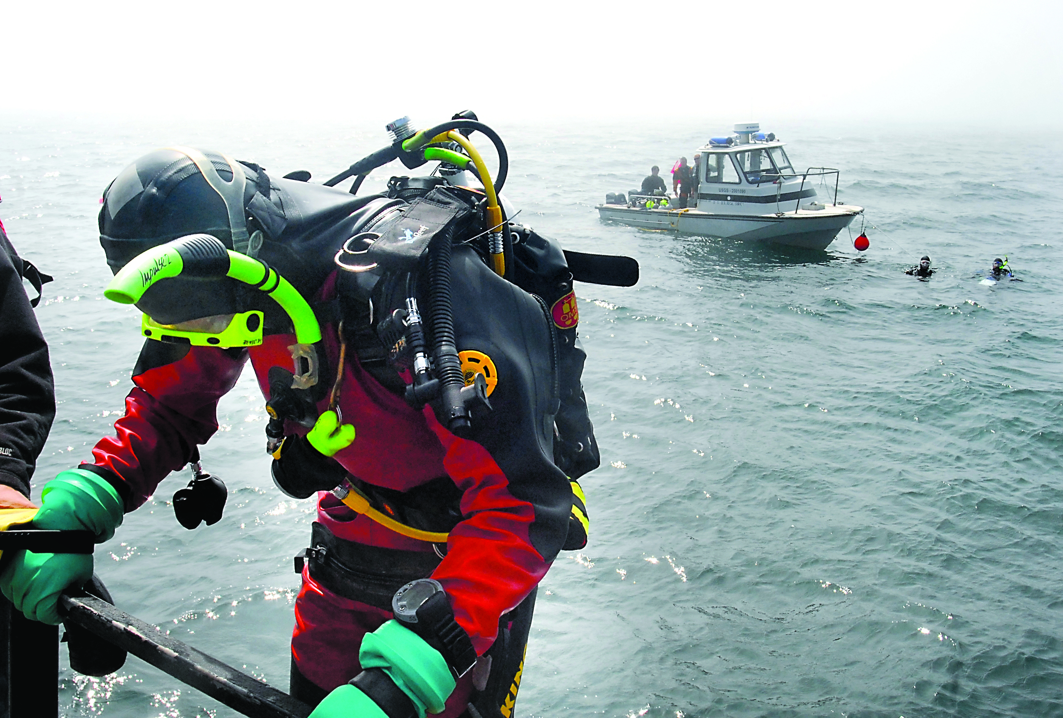 U.S. Environmental Protection Agency diving officer Sean Sheldrake prepares to enter the water as a dive team from the U.S. Geological Survey waits to meet up for a journey down to dive point “Charlie 2” in Freshwater Bay