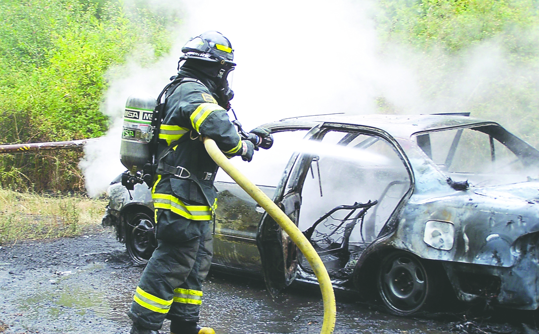 A Clallam County firefighter aims his hose at the sedan that burned west of Port Angeles on Saturday. Clallam County Fire District No. 2