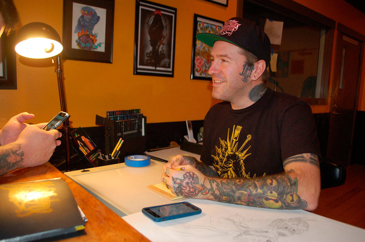Professional tattoo artist Keith Dulin discusses tattoo design concepts with a client during the official opening of his business, Black Reign Tattoo, on Nov. 25 in Sequim. (Erin Hawkins/Olympic Peninsula News Group)