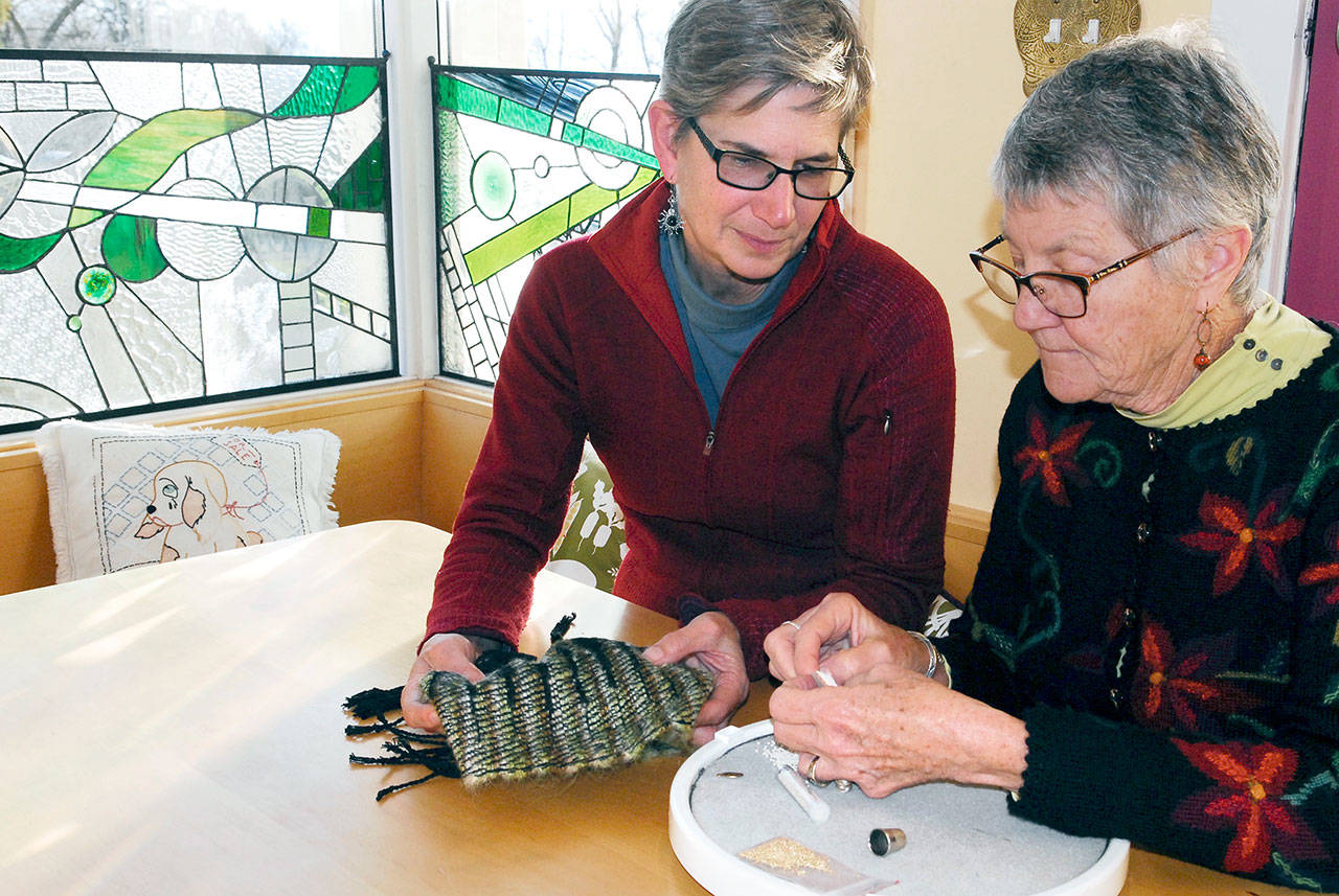 Weaver Cathie Wier, left, discusses Pat Herkal’s beaded embroidery piece for their collaboration. They will be part of the Chimacum Holiday Weekend on Saturday. (Jeannie McMacken/for Peninsula Daily News)