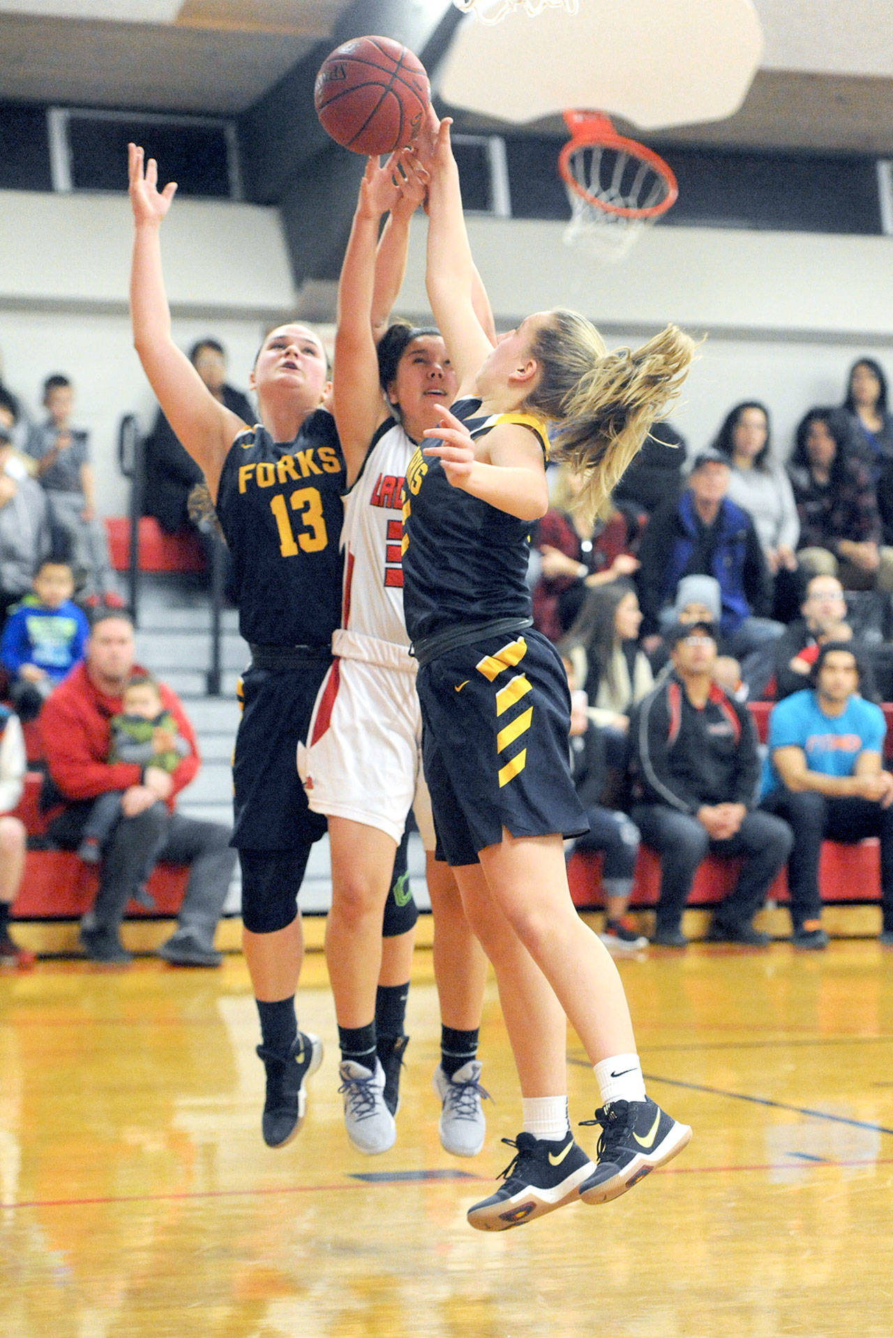 Lonnie Archibald/for Peninsula Daily News Forks’ Rian Peters (13) and Chloe Leverington compete with Neah Bay’s Ruth Moss (32) for the rebound during Neah Bay’s 53-39 win.