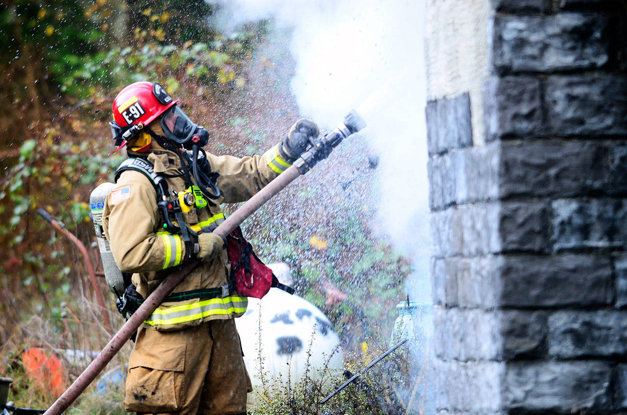A firefighter sprays down the Port Townsend-area home that caught fire Thursday morning. The couple living in the home escaped without injury. (Jesse Major/Peninsula Daily News)