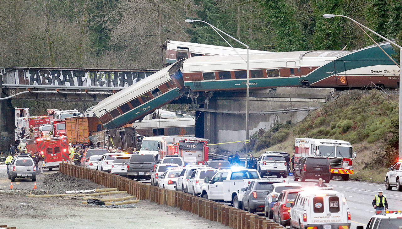 Cars from an Amtrak train lay spilled onto Interstate 5 as some remain on the tracks above Monday in DuPont. The Amtrak train making the first-ever run along a faster new route hurtled off the overpass early Monday near Tacoma and spilled some of its cars onto the highway below, killing several people, authorities said. Seventy-seven passengers and seven crew members were aboard when the train derailed about 40 miles south of Seattle before 8 a.m., Amtrak said. (Elaine Thompson/The Associated Press)