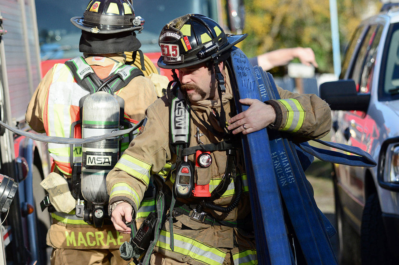 East Jefferson Fire-Rescue firefighter Zach Dean pulls a hose off a fire truck as he arrives at the scene of a house fire in Port Townsend on Wednesday. (Jesse Major/Peninsula Daily News)