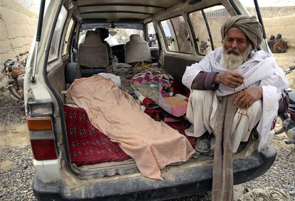 An elderly Afghan man sits next to the covered body of a person who was allegedly killed by a U.S. service member. The Associated Press