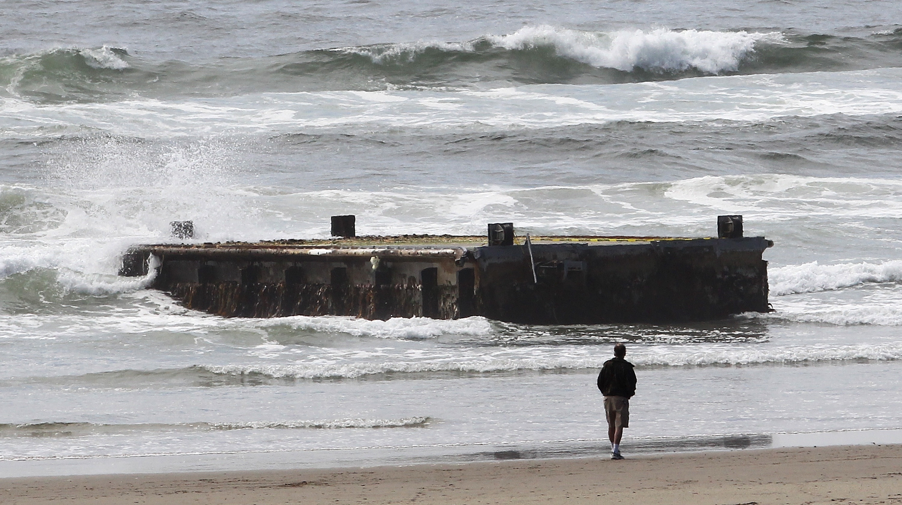 A man looks at the massive dock — a relic from 2011 Japanese tsunami — that washed ashore near Newport