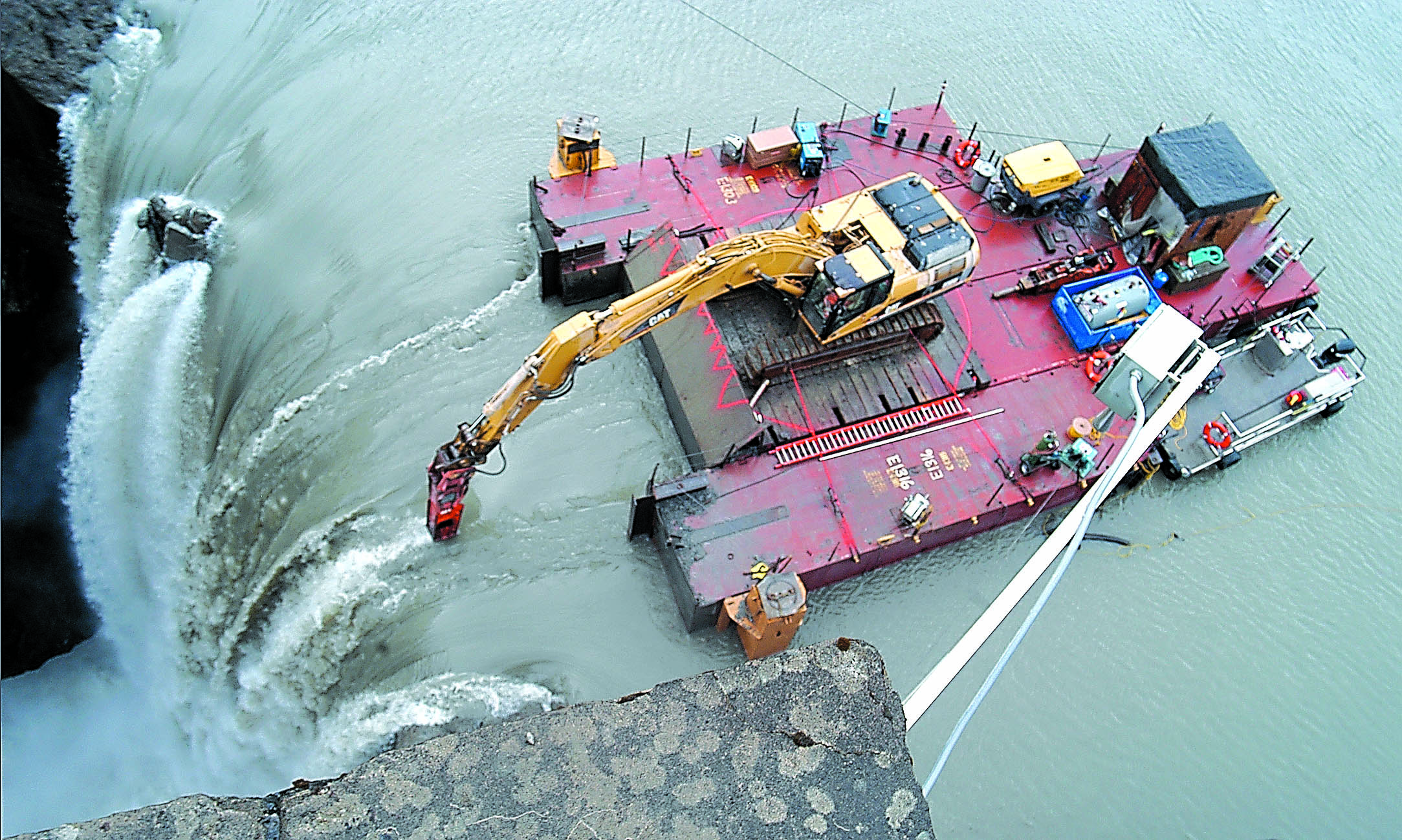 A tethered barge carrying an excavator with a jackhammer attachment chips away at the precipice as water flows over the Glines Canyon Dam.  -- Photo by Keith Thorpe/Peninsula Daily News