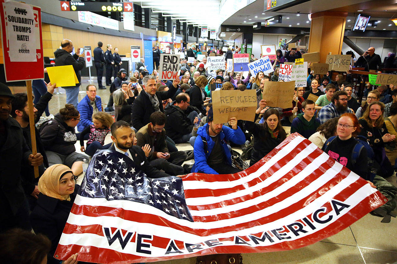 In this Jan. 28, 2017, file photo, demonstrators sit down in the concourse and hold a sign that reads “We are America,” as more than 1,000 people gather at Seattle-Tacoma International Airport to protest President Donald Trump’s order that restricts immigration to the U.S., in Seattle. (Genna Martin/seattlepi.com via AP, File)