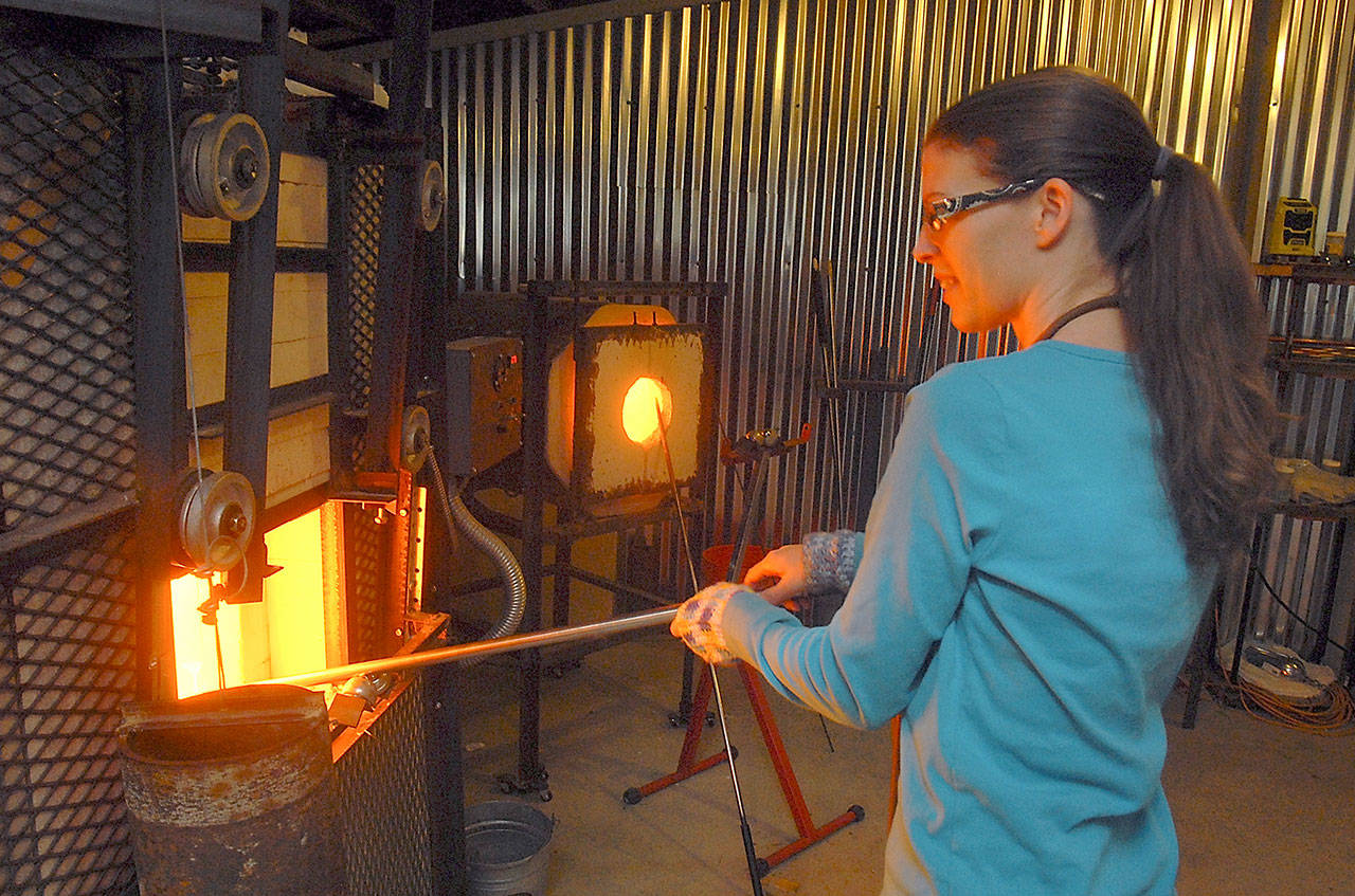 Megan Schimidlkofer collects molten glass from an oven in preparation for blowing a glass ornament at her Molten Momma’s Hot Shop glassworks in rural Sequim. (Keith Thorpe/Peninsula Daily News)
