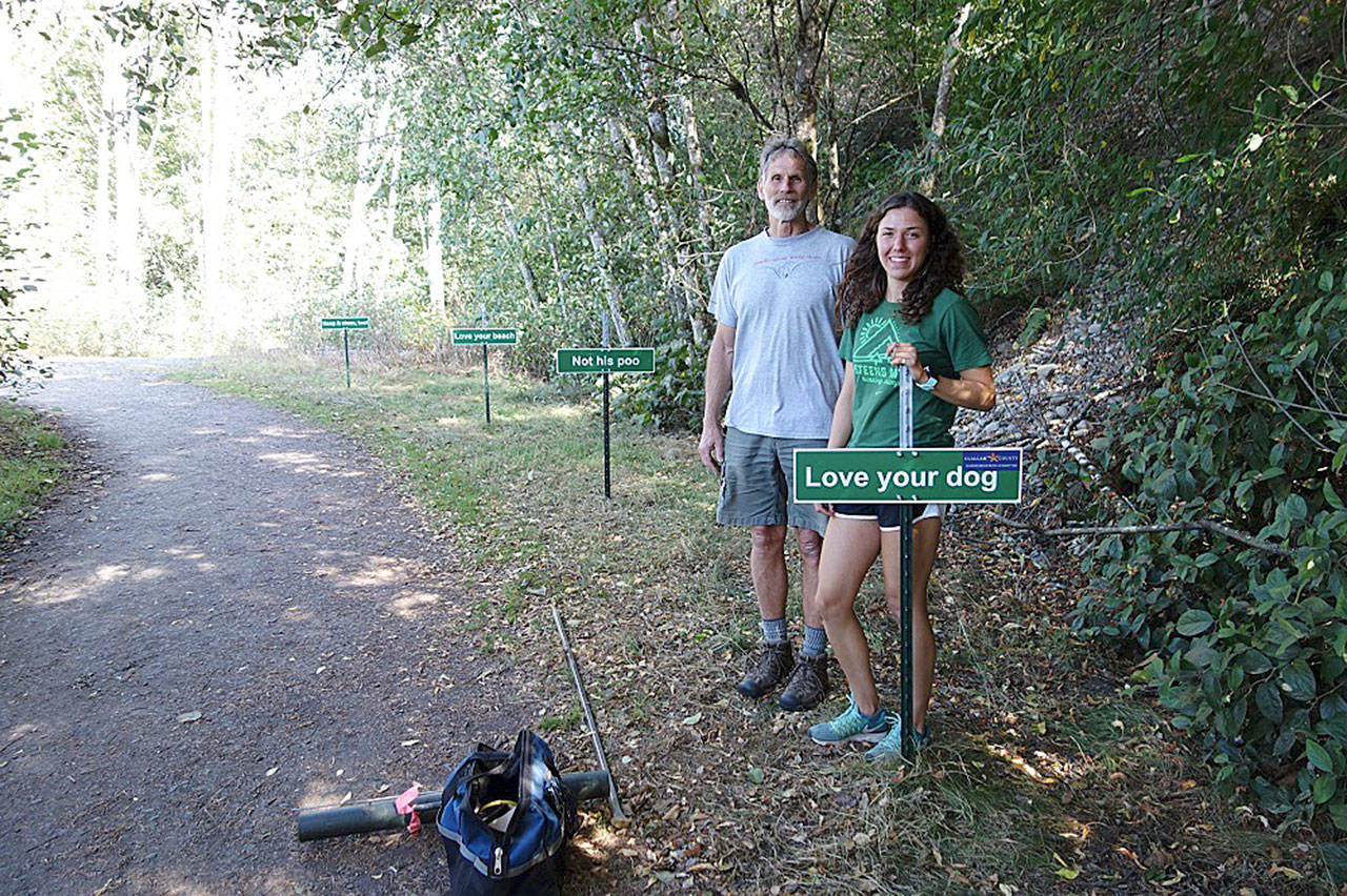 Arnold Schouten and Waverly Shreffler install a row of small humorous signs encouraging owners to pick up after their dogs.