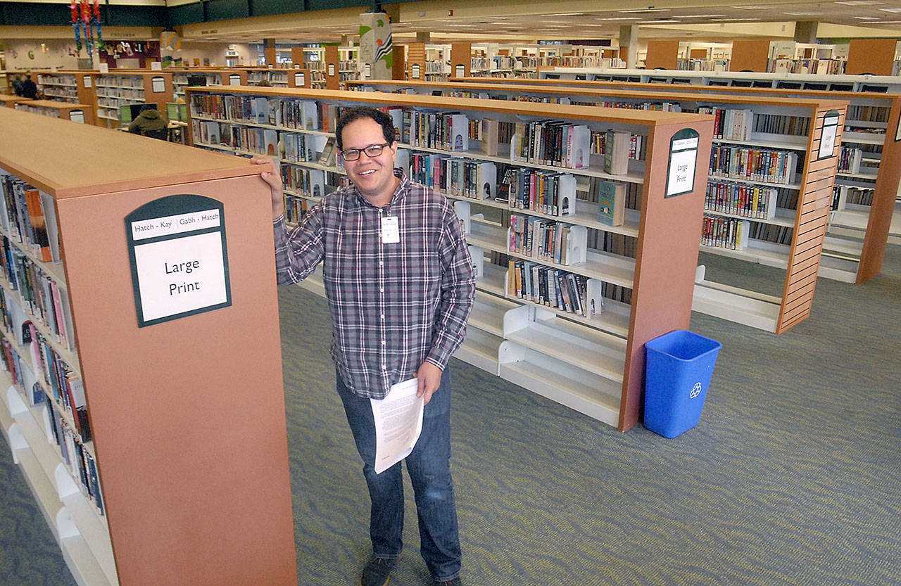 Noah Glaude, assistant library director for the North Olympic Library System, stands in the large print and periodical section of the Port Angeles Public Library, an area that has been designated for replacement carpeting in the library’s capital budget. (Keith Thorpe/Peninsula Daily News)