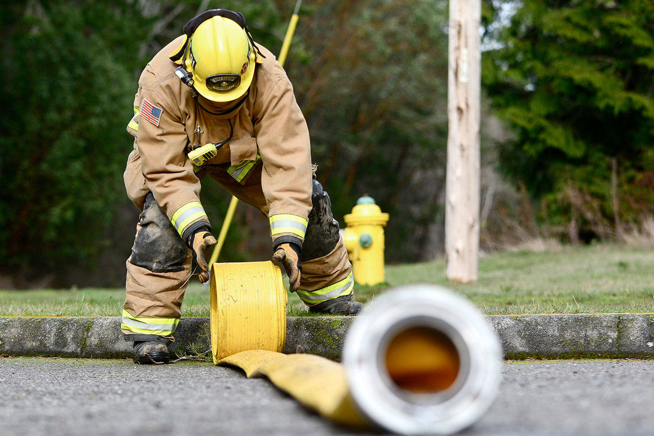 Firefighter Benjamin Richter rolls up a hose in front of the fire station at Naval Magazine Indian Island. (Jesse Major/Peninsula Daily News