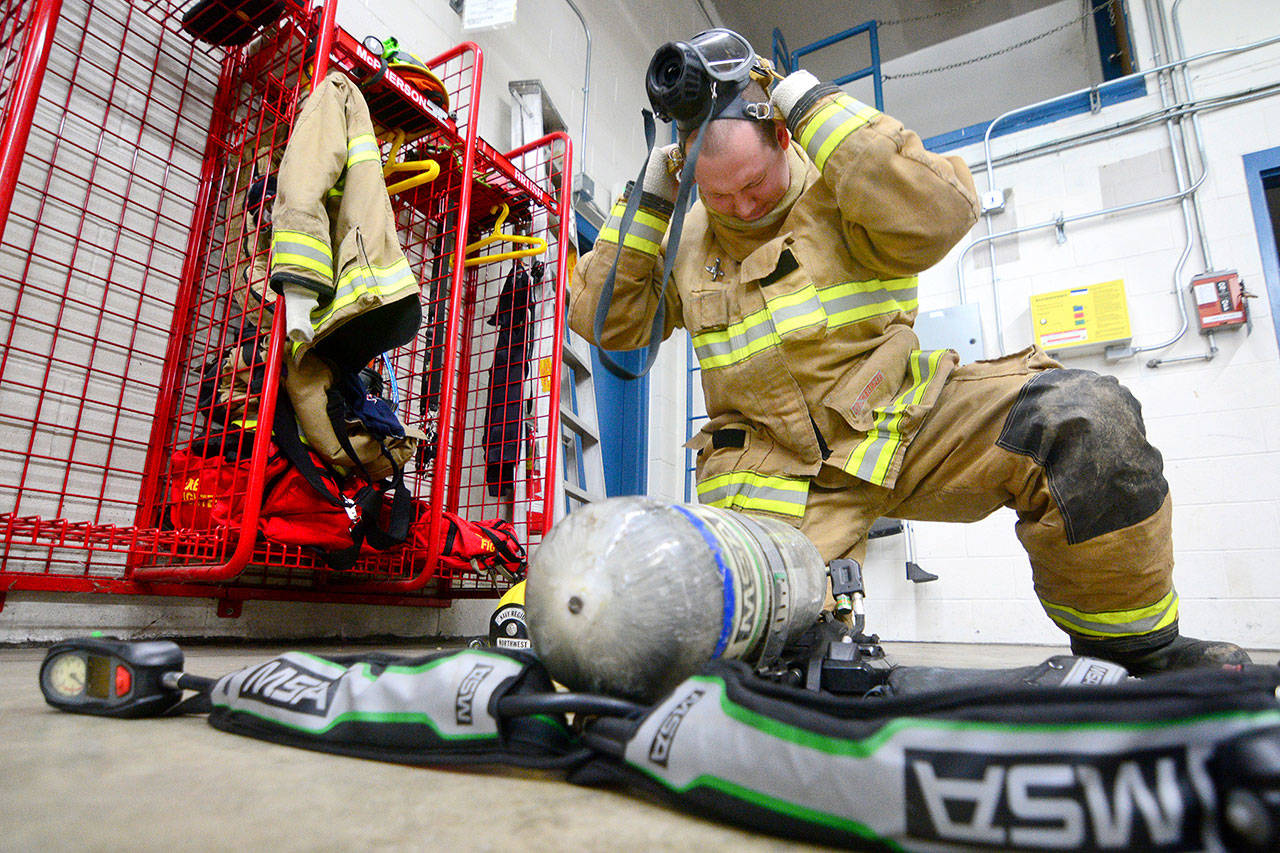 Firefighter Benjamin Richter demonstrates how quickly firefighters need to put on their gear when called out to an incident. (Jesse Major/Peninsula Daily News)